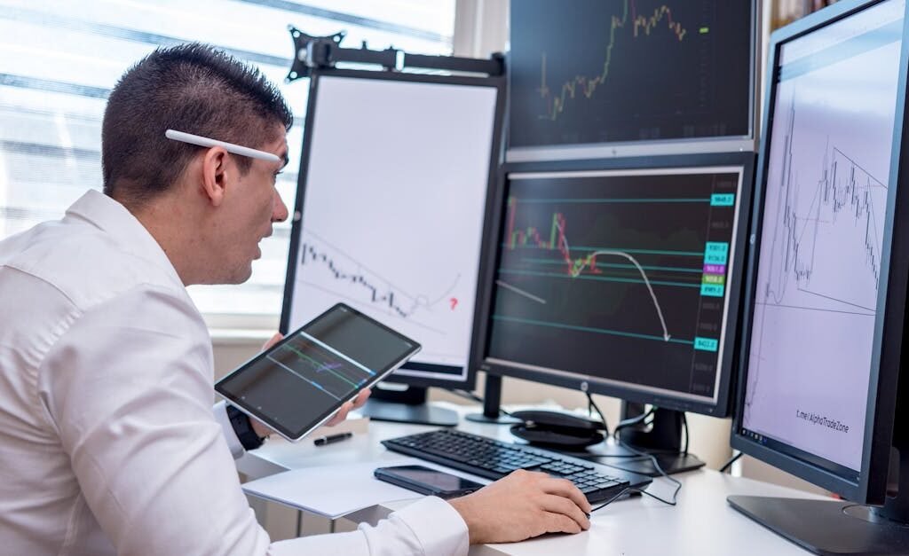 A man analyzing stock market graphs on multiple screens at a workstation.